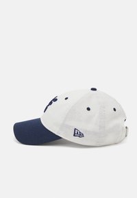 Cappello con corpo in tessuto bianco e visiera blu navy. Le caratteristiche includono un logo ricamato e dettagli con bottoni sulla parte superiore.