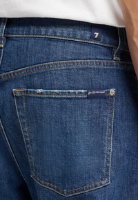 Denim jeans met een donkerblauwe tint, met contrasterende oranje stiksels, een achterzak met een genaaid label en een klassieke snit.