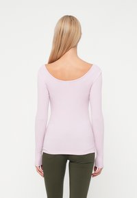 Top longo lilás de mangas largas com decote arredondado e textura canelada. O ajuste é justo, combinado com calças verde-oliva.