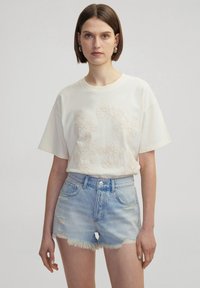 Crème T-shirt met korte mouwen en bloemenborduurwerk aan de voorkant, gecombineerd met lichtblauwe denim shorts met een rafelige zoom en versleten details.