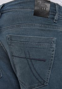 Blue denim jeans back pocket with dark stitched design and black leather brand patch reading Camp David on waistband.