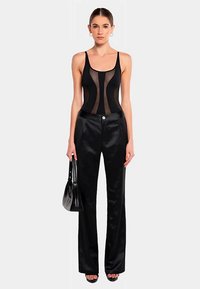 Svart bodysuit med genomskinliga paneler och en slät textur, kombinerad med svart högmidjade satintrosor, försedda med knapp och ficka.