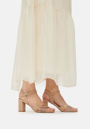 Béžové sandále na blokovom podpätku s úzkymi remienkami, s prackou a lesklým detailom na prstoch. Mäkko vyzerajúca koža s matným povrchom.