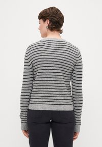 Stripet grå genser med svarte linjer, ribbestrikkede mansjetter og kant, myk tekstur, rund hals design, brukt med mørkegrå jeans.