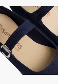 Bailarinas de tela azul marino con suela plana, que presentan un diseño de tiras entrelazadas y un detalle de hebilla metálica. Plantilla marrón con el logo de la marca.