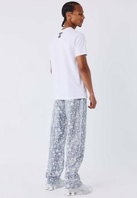 T-shirt en coton blanc avec un motif au dos, associé à un pantalon ample à motifs bleus clairs présentant des motifs tropicaux et une silhouette décontractée.
