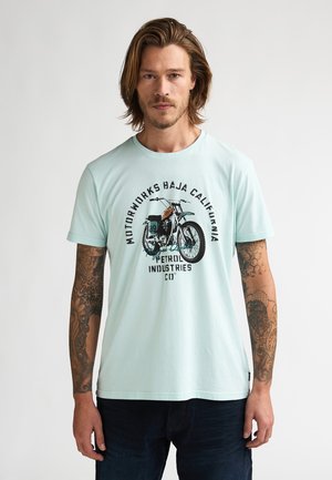 Mintgroen katoenen T-shirt met een motorfietsafbeelding en tekst. Korte mouwen, ronde hals, losse pasvorm en zichtbare tatoeageontwerpen op de arm.