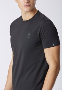 T-shirt nera a maniche corte in cotone, con un piccolo logo scuro sul lato sinistro del petto e un accento sottile sulla manica.