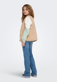 Beežist fliisvest mintroheliste ja valgete pikkade varrukatega, stiliseeritud siniste laiade teksapükstega ja mustade tennistega, ees nupud ja lõdva lõikega.