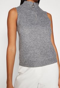 Grijs mouwloos topje met een hoge kraag en een rits aan de voorkant, gemaakt van ribstof, met een aansluitende pasvorm en een zachte textuur.
