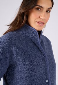 Marineblauwe fleecejas met een gestructureerde oppervlakte, staande kraag en drukknoopsluitingen. Heeft een gladde afwerking langs de randen.