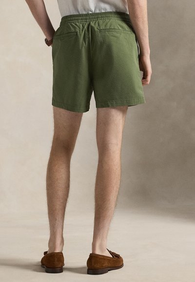 Πράσινα σορτς με υφή, με ελαστική μέση, δύο πίσω τσεπάκια και άνετη εφαρμογή, σε συνδυασμό με καφέ μοκασίνια από σουέτ.