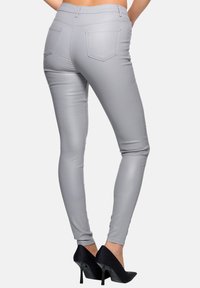 Graue, schlanke Hose aus glattem, elastischem Material, mit Gesäßtaschen und anliegender Form, kombiniert mit schwarzen High Heels.