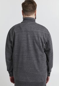 Grå, texturerad tröja med hög krage, långa ärmar samt ribbad mudd och nederkant. Tyget verkar mjukt och något borstat.