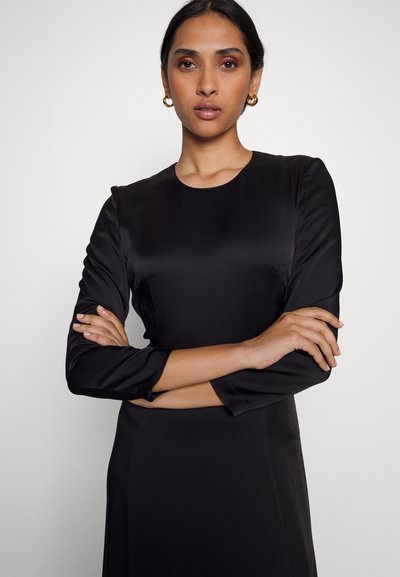 Mustmust kleit ümmarguse kaelusega ja kolmveerandvarrukatega. Kangas on sileda tekstuuriga ning minimaalsete detailidega.