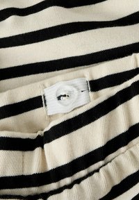 Bouton réglable avec boutonnière sur une ceinture en tissu tricoté à rayures crème et noir.