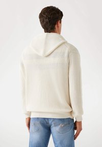 Strick-Hoodie in Cremefarbe, mit geripptem Design, überschnittenen Schultern und lockerer Passform. Getragen zu hellblauen Jeans.