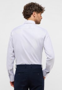Camicia a maniche lunghe azzurro chiaro con colletto strutturato e una sottile trama, abbinata a pantaloni eleganti blu navy con tasche posteriori e dettagli in bottone.