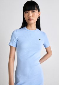 Robe légère bleu clair à manches courtes et côtelées, avec un col rond, une coupe ajustée et un petit logo crocodile vert foncé sur la poitrine.