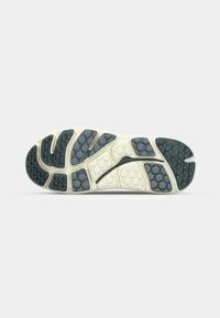 Semelle extérieure d'une chaussure de course avec une base blanche et des motifs hexagonaux gris foncé pour l'adhérence et la flexibilité.