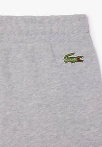 Pantalons de survêtement en coton gris avec une taille élastique. Présente un petit logo de crocodile brodé en vert près de la taille.