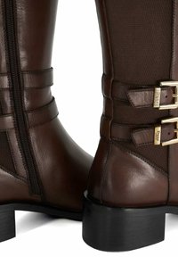 Brown leather ankle boots with textured side panels, gold-tone hardware buckles, a zip closure, and block heels.