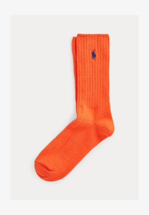 Svijetlo narančasta rebrasta čarapa s plavim vezanim logotipom jahača polo na manžeti na bijeloj pozadini.