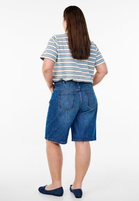 Denim šorti ar brīvu piegriezumu, vidēji zila krāsā, ar izsistiem malām. Kombinēti ar īsu, svītrainu, īsām piedurknēm t-kreklu.