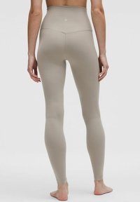 Hoch geschnittene Leggings in einem hellen Beigeton, mit glatter Textur, enganliegendem Schnitt, vollständiger Beinabdeckung und einem diskreten Logo auf der Rückseite.