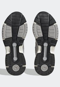 Sneakersålar med en kombination av svart och grå gummi, texturerade mönster för bättre grepp och en central vridkomponent för stöd.