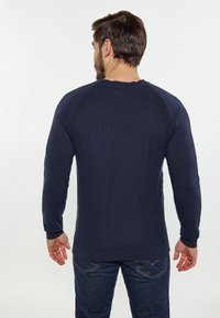 Marineblauwe lange mouw sweater van textuurstof, met ribbels aan de manchetten en onderkant. Achteraan zichtbaar met raglanmouwen en een ontspannen pasvorm. Draag met blauwe jeans.