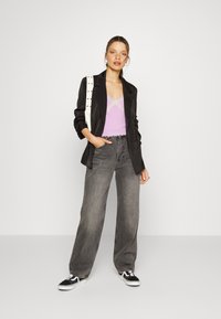 Blazer preto sobre uma blusa sem mangas lilás com rendas, combinado com jeans cinzentos de perna larga de cintura alta e ténis preto e branco. Mala de lona com studs.