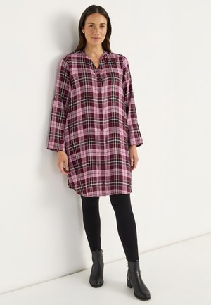 Kragenhemdkleid im rosa-lila Karomuster, mit geknöpftem Frontteil, langen Ärmeln. Getragen mit schwarzen Leggings und Stiefeletten.