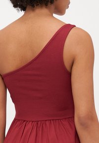 Vestido burdeos con un top asimétrico acanalado que tiene una amplia tira y una falda fluida y recogida. Textura suave en toda la prenda.