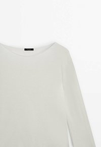 Haut à manches longues en écru, doté d'un large col et d'une texture douce. Le tissu semble léger et légèrement extensible.