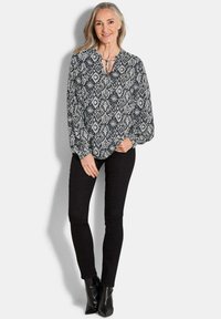 Langärmlige Bluse im marineblauen und weißen Muster mit V-Ausschnitt und Bindeschluss. Kombiniert mit schwarzen Skinny-Jeans und Stiefeletten.