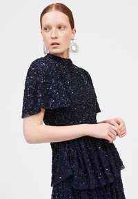 Vestido de lentejuelas azul marino con cuello alto y mangas cortas, que presenta capas de volantes y detalles intrincados.