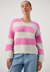 Maglione lavorato a maglia con righe orizzontali rosa e bianche, design over-size, scollatura rotonda, orlo a costine e tessuto texture. Abbinato a jeans blu.
