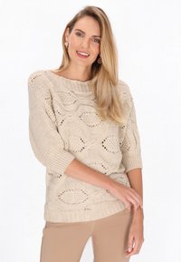Pulover bej tricotat cu un model texturat în valuri, guler larg și mâneci trei sferturi, asortat cu pantaloni bej deschis.