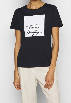 Czarna bawełniana koszulka z krótkim rękawem i okrągłym dekoltem, z białym kwadratowym nadrukiem i czarnym odręcznie napisanym tekstem "Tommy Hilfiger."