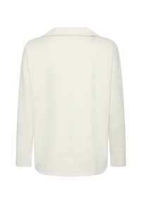 Ilgų rankovių, off-white marškiniai su plačiu apykakle, matomais siūlių detalėmis ant rankovių ir subtiliu prekės ženklu netoli apatinio krašto gale.