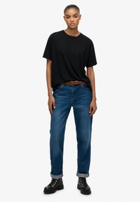 Sort crew-neck t-shirt parret med lyseblå, lige bukser, sikret med et brunt fletbælte og sorte snørestøvler.