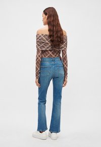 Top marrón a cuadros con escote off-the-shoulder combinado con jeans azules de tiro medio y corte recto, y zapatillas blancas. Los jeans tienen bolsillos traseros y un acabado texturizado.