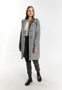 Lys grå uldblandingsfrakke med hætte, stroplukninger og knapdetaljer, parret med sorte slim-fit jeans og sorte ankelstøvler.