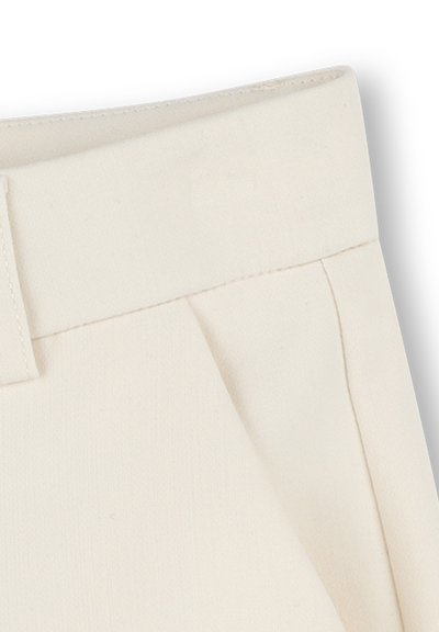 Pantalons de couleur crème avec une large ceinture, un devant plissé et un tissu doux et texturé. Pas de matériel ou de motifs visibles.