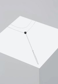 Sølvhalssmykke med to kæder, der har en rund sort sten som midtpunkt og en lang, spids vedhæng for et lagdelt, geometrisk design.