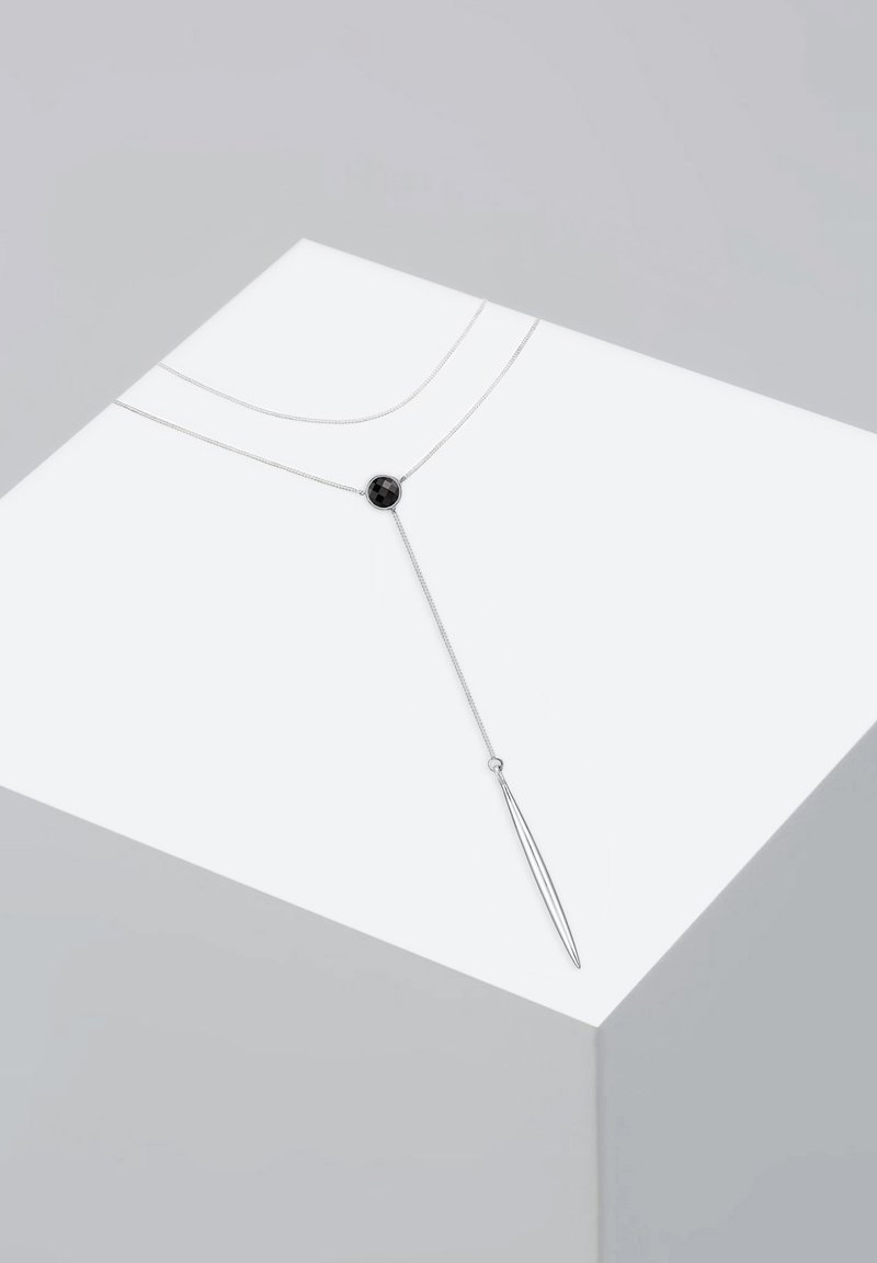 Sølvhalssmykke med to kæder, der har en rund sort sten som midtpunkt og en lang, spids vedhæng for et lagdelt, geometrisk design.