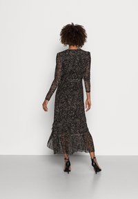 Langes schwarzes Kleid mit transparenten langen Ärmeln und einem gestuften Rüschensaum. Verfügt über ein geometrisches Muster in hellbraun. Enganliegend in der Taille.