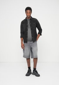 Mustast teksariidest särk halli t-särgi kohal, kombineeritud hallide teksapükstega ja mustade tennistega. Lihtne disain, istuv lõige, nähtavad õmbluse detailid.