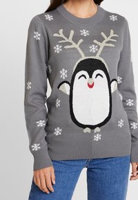 Harmaa neule, jossa on pingviinimuotokuva, joka on koristeltu sarvilla, hymyilevällä kasvoilla ja lumihiutaleilla. Ribba jotka hihansuissa ja helmassa.